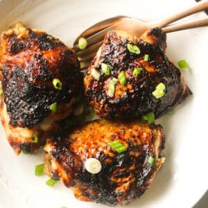 bbq chicken thighs with sliced green onions on top on a white plate