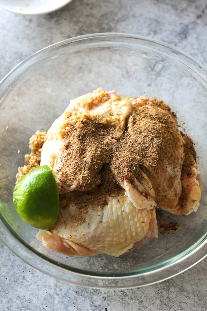 lime and jerk seasoning on top of chicken thighs in a glass bowl