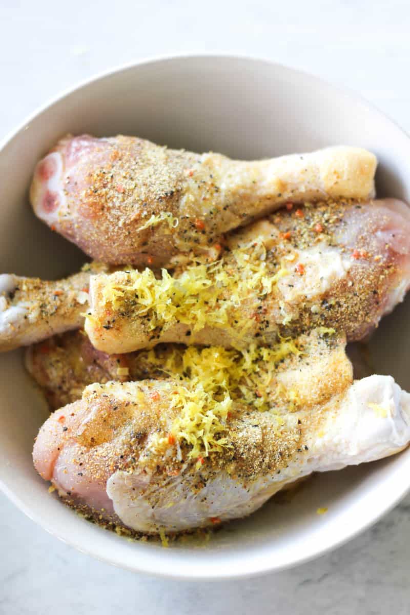 seasoning and lemon zest on top of chicken drumsticks in the bowl
