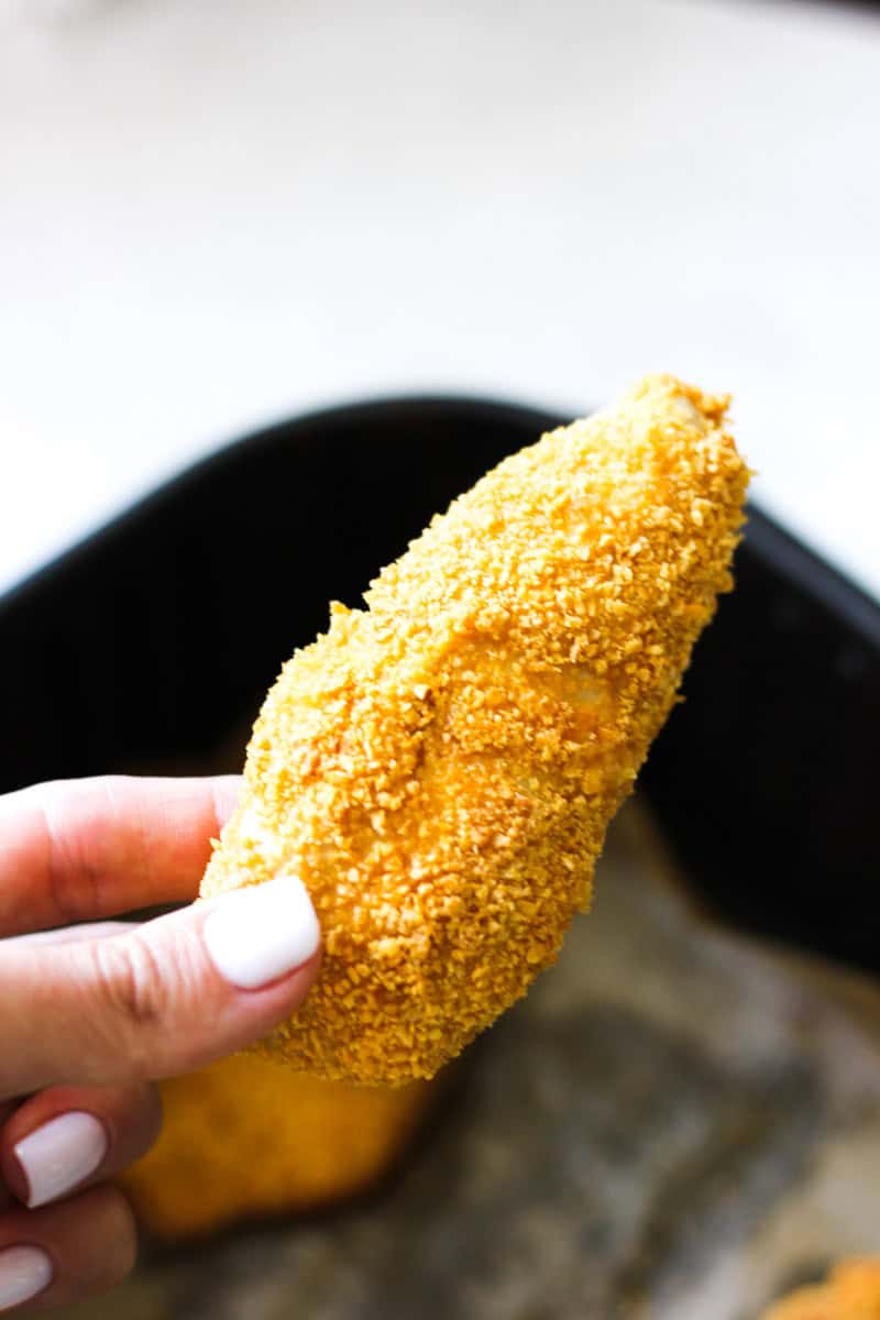 holding a chicken tender covered with crumbed corn flakes