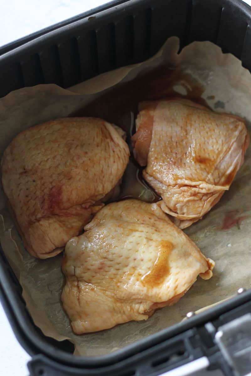 three chicken thighs covered in sauce in the air fryer basket